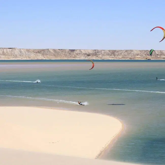 Cztery osoby uprawiają kitesurfing na lagunie wśród piasków i klifów - idealny spot na wakacje z kitesurfingiem KiteAway.