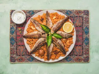 Talerz ryżu z grillowaną rybą i dodatkami na kolorowej macie, idealny po kite campie lub wakacjach z kitesurfingiem z KiteAway.