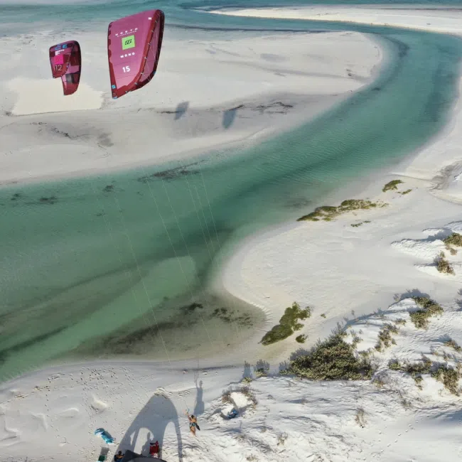 Dwóch kitesurferów z różowymi latawcami na turkusowej wodzie przy białych wydmach-idealny obóz latawcowy KiteAway.