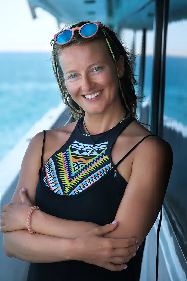 Uśmiechnięta kobieta w kostiumie na łodzi, gotowa na kite trip z KiteAway - wyjazdy kitesurfingowe, wakacje z kitesurfingiem.