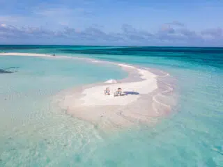 Mała, piaszczysta wyspa otoczona turkusową wodą i leżakami, idealna na wyjazdy kitesurfingowe z KiteAway pod błękitnym niebem.