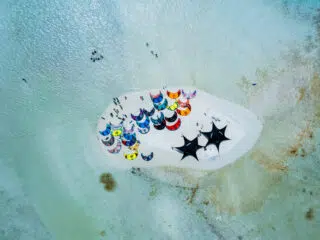 Widok z lotu ptaka na kite spot KiteAway - kolorowe latawce, grupy kitesurferów i namioty podczas wyjazdu kitesurfingowego.
