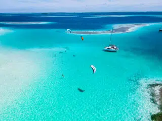 Turkusowa laguna z kitesurferami i katamaranem; idealne wakacje z kitesurfingiem z KiteAway na egzotycznym kite spocie.