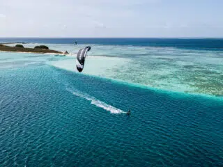 Kitesurfer na tle lazurowej wody i rafy koralowej, idealny kite spot na wyjazdy kitesurfingowe z KiteAway.pl.
