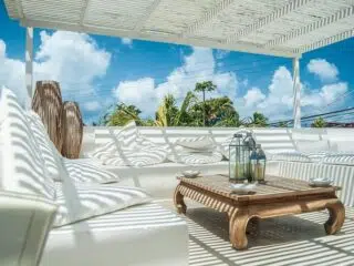 Biały salon z poduchami, stolik z drewna, pergola i palmy-idealne miejsce na relaks po wyjazdach kitesurfingowych KiteAway.