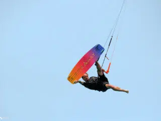 Kitesurfer wykonuje trip w powietrzu na wyjeździe kite z KiteAway, trzymając kolorową deskę, idealny kite trip na wakacje z kitesurfingiem.