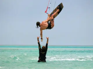 Kitesurfer wykonuje trik nad turkusową wodą podczas wyjazdu kitesurfingowego KiteAway, w tle kite spot i spokojne morze.