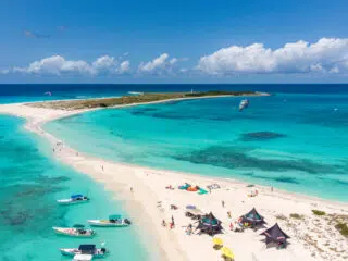 Plaża z białym piaskiem i lazurową wodą, kitesurferzy na tle kite campu KiteAway, idealne miejsce na wyjazdy kitesurfingowe.