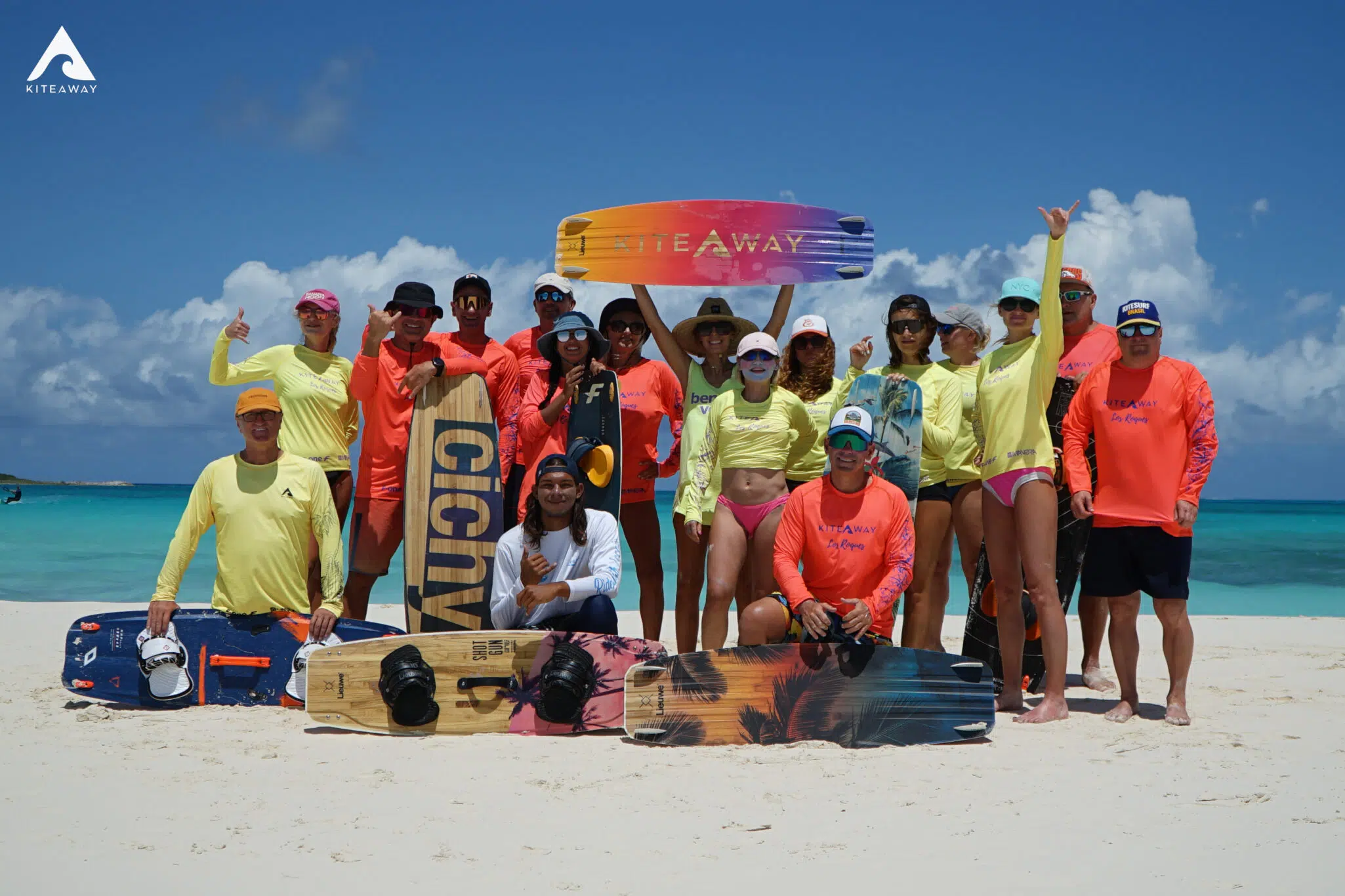 Uśmiechnięta grupa w żółtych i pomarańczowych koszulkach na plaży z deskami, KiteAway - wakacje z kitesurfingiem. Uśmiechnięta grupa w żółtych i pomarańczowych koszulkach na plaży z deskami, KiteAway - wakacje z kitesurfingiem.