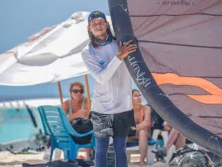 Uczestnik kite campu KiteAway w stroju plażowym z latawcem, plaża, relaksujące osoby; idealny wyjazd kitesurfingowy nad morzem.