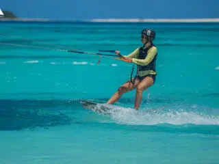 Osoba w kasku uprawiająca kitesurfing na turkusowej wodzie podczas wyjazdu KiteAway; idealne miejsce na kite camp i szkolenie kite.