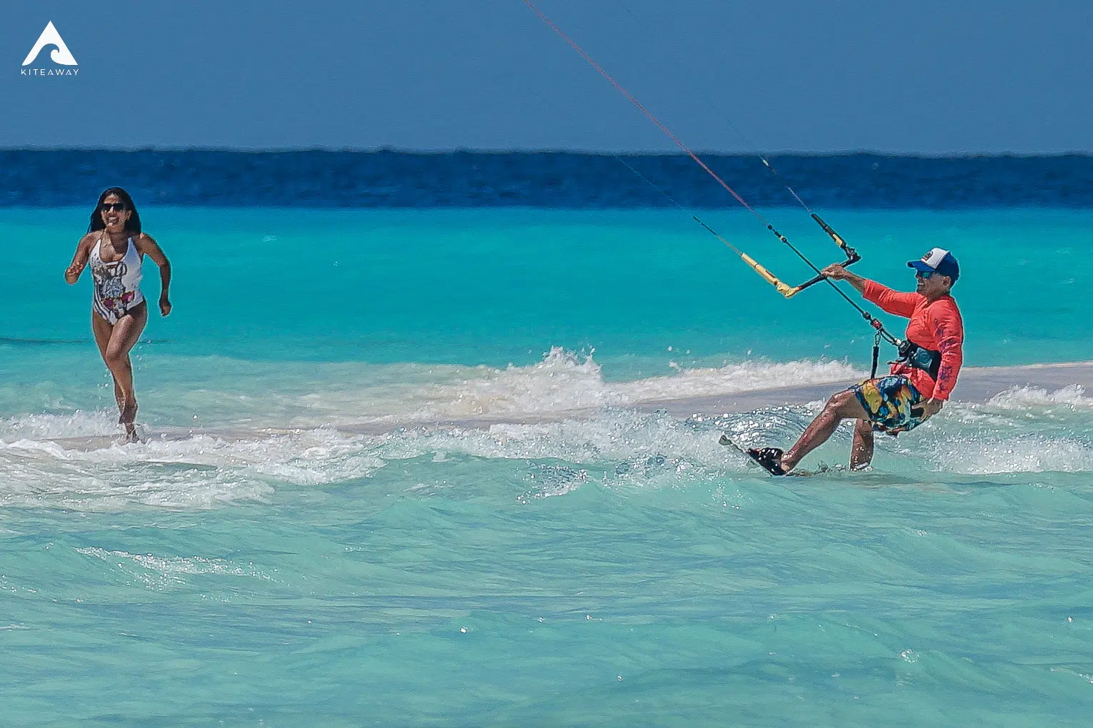 Mężczyzna na kitesurfingu w turkusowej wodzie, kobieta biegnie plażą - wakacje z kitesurfingiem KiteAway, kite camp. Mężczyzna na kitesurfingu w turkusowej wodzie, kobieta biegnie plażą - wakacje z kitesurfingiem KiteAway, kite camp.