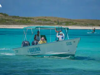 Motorówka Varuna na turkusowej wodzie przy plaży, w tle kitesurfing-idealny spot na wyjazdy kitesurfingowe z KiteAway.
