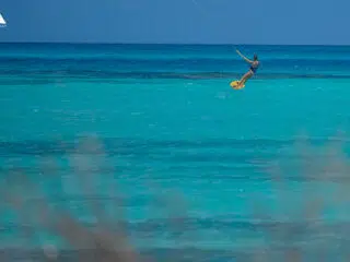 Kitesurfer sunący po turkusowej wodzie podczas wyjazdu kitesurfingowego KiteAway; wakacje z kitesurfingiem, niebo i fale w tle.