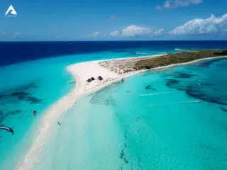 Widok z lotu ptaka na kite spot z białą plażą, turkusową wodą i kitesurferami - idealne miejsce na wyjazdy kitesurfingowe KiteAway.