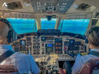 Dwóch pilotów w kokpicie samolotu leci nad lazurowym oceanem na kite camp z KiteAway - wyjazdy kitesurfingowe pełne przygód.