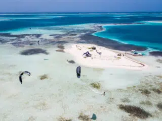 Mała, piaszczysta wyspa otoczona turkusową wodą, kitesurferzy na wyjeździe KiteAway, łodzie; idealny kite spot na wakacje z kitesurfingiem.