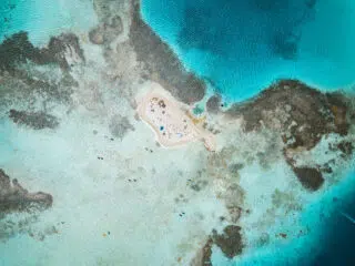 Mała piaszczysta wyspa otoczona turkusową wodą i rafami; grupa osób podczas kite campu KiteAway, idealny spot na wyjazdy kitesurfingowe.