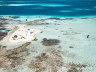 Mała piaszczysta wyspa z ludźmi i namiotami na tle turkusowej wody - idealna na wyjazdy kitesurfingowe KiteAway.