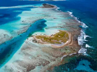 Widok z lotu ptaka na sercowatą wyspę z turkusową wodą i rafami-idealny kite spot na wyjazdy kitesurfingowe z KiteAway.