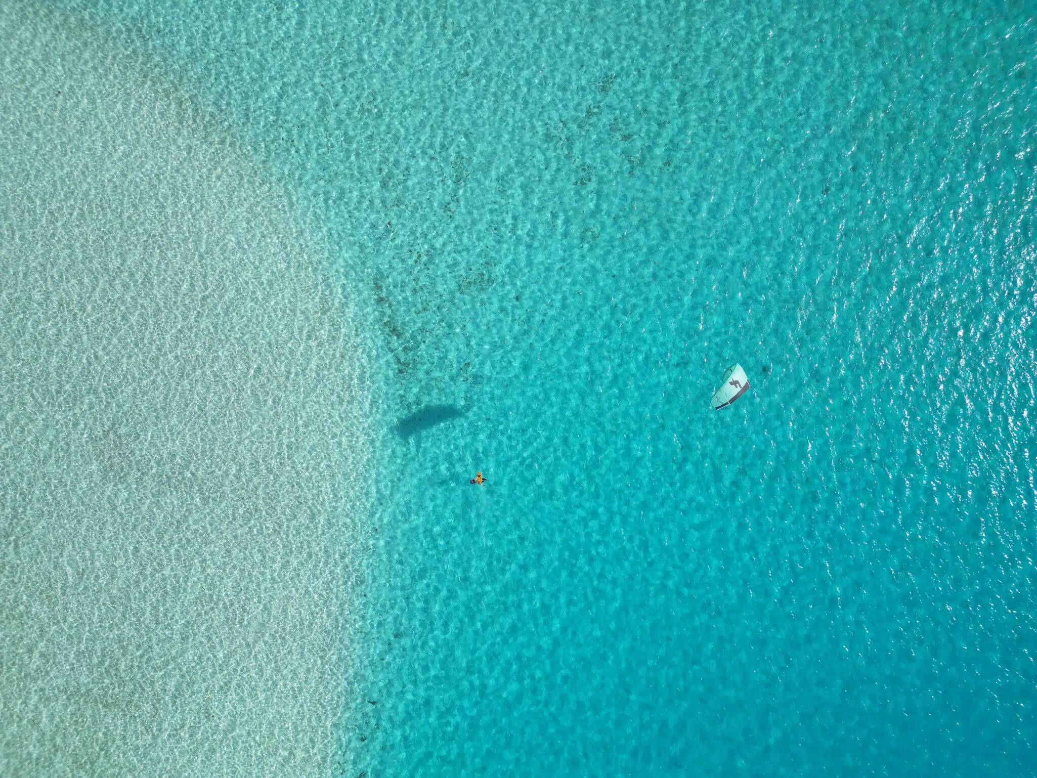 Z lotu ptaka: łódka i kitesurfer na turkusowej wodzie przy piaszczystym kite spocie - idealne na wyjazdy kitesurfingowe z KiteAway.