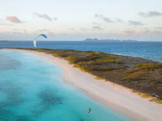 Kitesurfer na turkusowej wodzie przy piaszczystej plaży - idealny spot na wyjazdy kitesurfingowe z KiteAway.