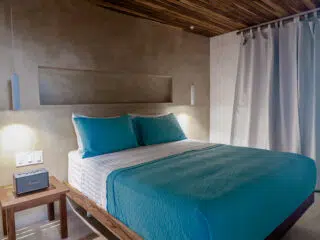 Nowoczesna sypialnia z drewnianym sufitem i turkusową pościelą - idealna po wyjeździe na kite camp KiteAway lub wakacje z kitesurfingiem.
