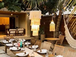 Stół z drewnianymi krzesłami pod palmami na kite campie KiteAway; wakacyjny klimat i relaks po wyjazdach kitesurfingowych.