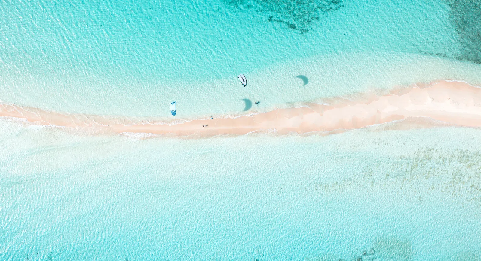 Widok z lotu ptaka na piaszczystą ławicę na turkusowym kite spocie, łodzie i kitesurferzy - idealne na wyjazdy kitesurfingowe z KiteAway.