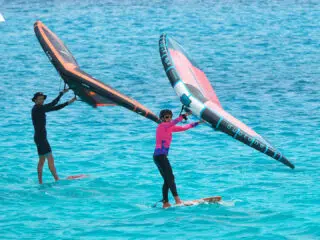 Dwie osoby uprawiają wing foil na turkusowej wodzie podczas wyjazdu kitesurfingowego KiteAway - wakacje z kitesurfingiem.