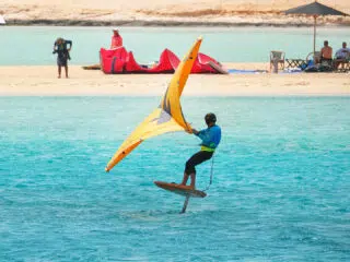 Kitesurfer na desce hydrofoil z żółtym żaglem ślizga się po turkusowej wodzie podczas wyjazdu kitesurfingowego KiteAway.