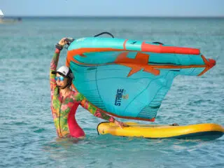 Osoba w kolorowej piance z żaglem wing foil na żółtej desce w turkusowej wodzie - idealne wyjazdy kitesurfingowe KiteAway.