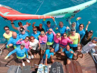 Uśmiechnięta grupa na pokładzie łodzi z deskami SUP, podczas wyjazdu kitesurfingowego KiteAway; turkusowa woda w tle.