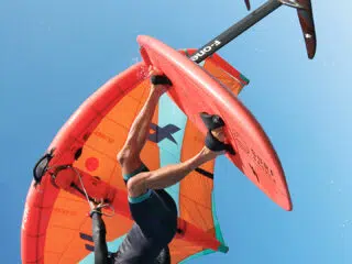 Kitesurfer w piance unosi się na wodolotach z pomarańczowym skrzydłem - wyjazdy kitesurfingowe z KiteAway, wakacje z kitesurfingiem.