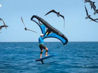 Osoba w kasku na niebieskiej koszulce pływa na hydroskrzydle z żaglem podczas wyjazdu kitesurfingowego KiteAway na morzu.