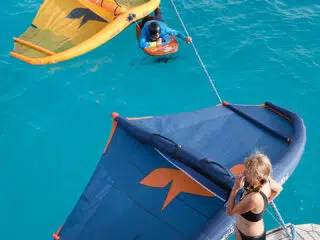 Dziewczyna w stroju kąpielowym na pomoście z latawcem, obok kursant na wodzie podczas wyjazdu kitesurfingowego KiteAway.