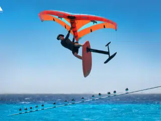 Kitesurfer skacze na czerwonym wodolocie z pomarańczowym skrzydłem na błękitnym morzu podczas wyjazdu kitesurfingowego KiteAway.