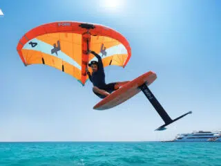 Uczestnik wyjazdu KiteAway pływa na wodolotach po turkusowej wodzie, trzymając latawiec. Idealny wyjazd i wakacje z kitesurfingiem.