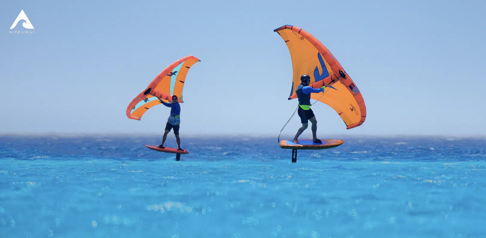 Dwóch kitesurferów na pomarańczowych wing foilach nad błękitnym morzem; KiteAway - wyjazdy kitesurfingowe, kite camp.