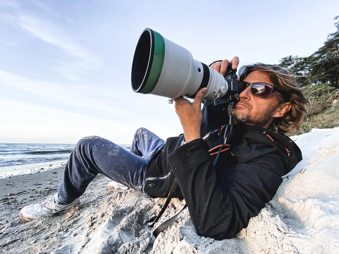 Osoba w okularach przeciwsłonecznych leży na plaży podczas wyjazdu kitesurfingowego KiteAway, fotografując kite spot.