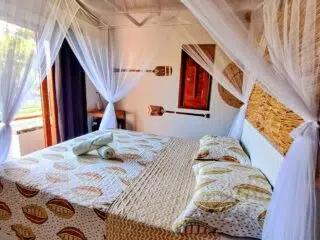 Przytulna sypialnia podczas wakacji z kitesurfingiem: duże łóżko pod moskitierą, słońce i kalkulator - relaks po KiteAway.