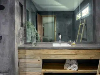 Nowoczesna łazienka po kite campie - betonowe ściany, drewniana umywalka, ręczniki, roślina i lustro. Idealne po wyjazdach kitesurfingowych.