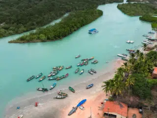 Lazurowa rzeka, łodzie przy piaszczystej plaży, zielone drzewa i dom-idealny kite spot na wyjazdy kitesurfingowe z KiteAway.