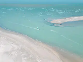Turkusowe morze z piaszczystymi łachami i kitesurferami na tle błękitnego nieba - idealny spot na wyjazdy kitesurfingowe z KiteAway.