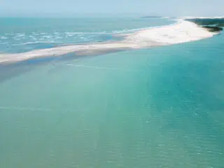 Widok z lotu ptaka na piaszczysty kite spot otoczony turkusową wodą, idealny na wyjazdy kitesurfingowe z KiteAway.