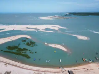 Plaża z turkusową wodą, kite camp KiteAway, wyjazdy kitesurfingowe i kitesurferzy na tle błękitnego nieba i wysp.