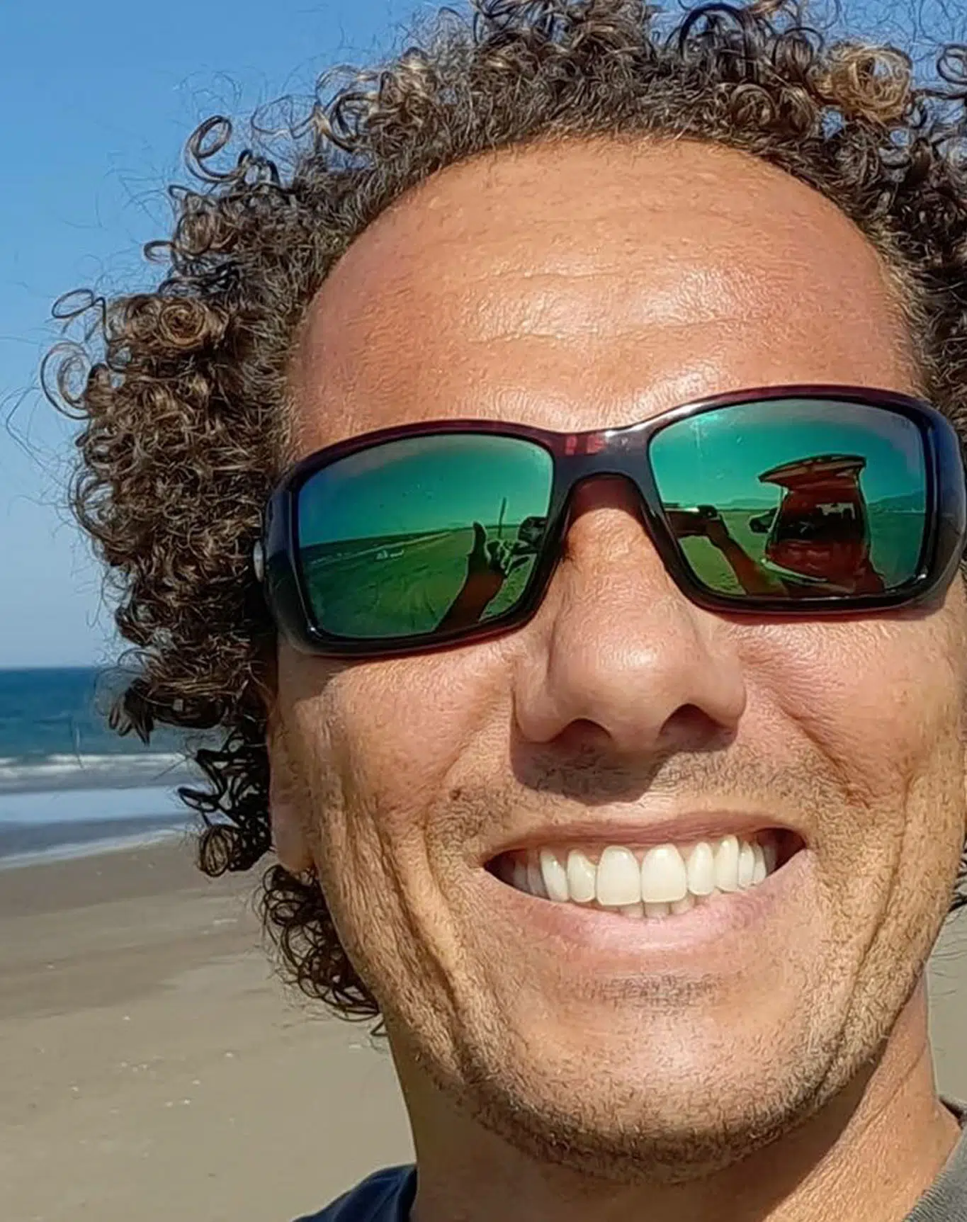 Uśmiechnięty mężczyzna w koszulce KiteAway pokazuje shaka na łodzi podczas wyjazdu kitesurfingowego nad turkusową wodę.