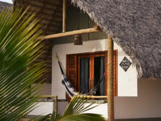 Przytulny bungalow z hamakiem na tarasie, idealny na wyjazdy kitesurfingowe z KiteAway; w tle roślina i tabliczka z napisem.