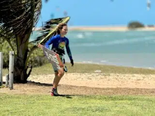 Kitesurfer z deską idzie po trawie blisko plaży na KiteAway kite camp - idealne miejsce na wyjazdy kitesurfingowe i kite trip.