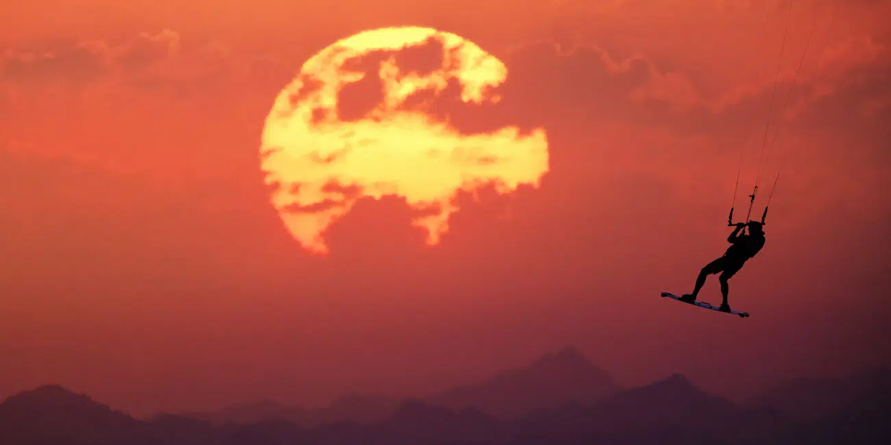 Sylwetka kitesurfera na tle pomarańczowego zachodu słońca - idealna scena na wyjazdy kitesurfingowe z KiteAway.